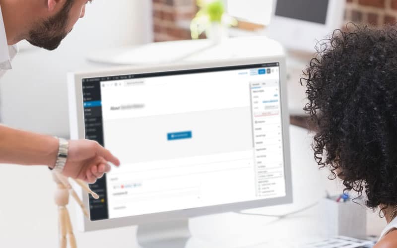 A man showing a woman how to edit a small business website design by pointing to the screen while she sits at the desk